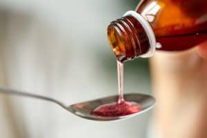 A person measures calories in cough syrup by pouring a bottle of cough syrup into a spoon.