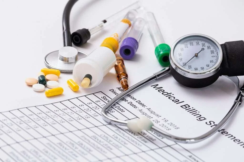 Pills, blood pressure gauge and medical billing statement representing the Eliquis co-pay card for insured patients