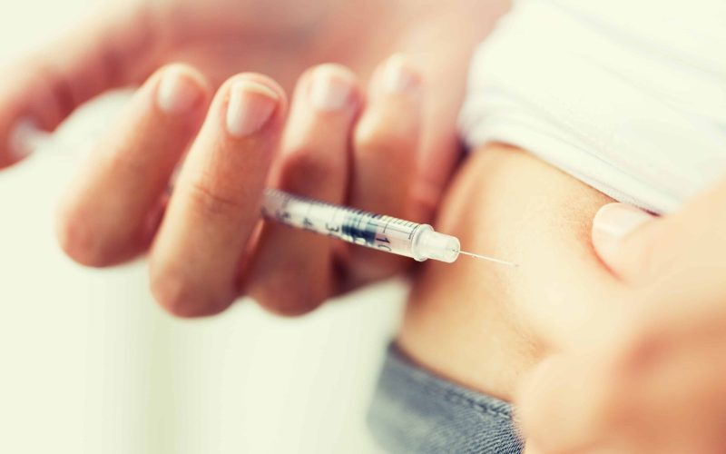 medicine, diabetes, glycemia, health care and people concept - close up of woman with syringe making insulin injection to himself at home