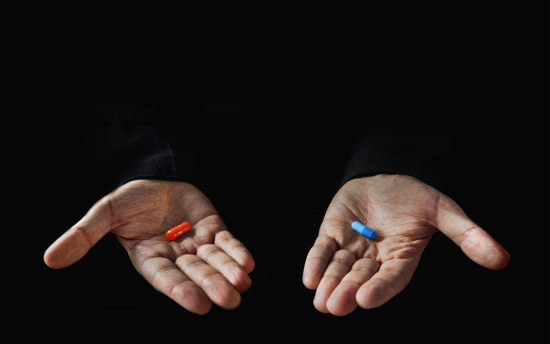 Red and blue pills on hand isolated on black background