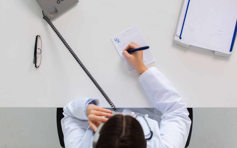 medicine, healthcare and people concept - doctor with prescription calling on phone at table in clinic