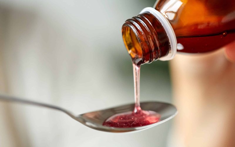 healthcare, treatment and medicine concept - bottle of medication or antipyretic syrup and spoon