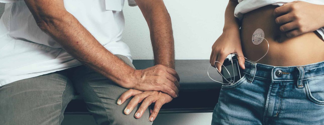 Cropped view of a young diabetic patient is keeping in his pocket an insulin pump in the doctor office. Child diabetes concept