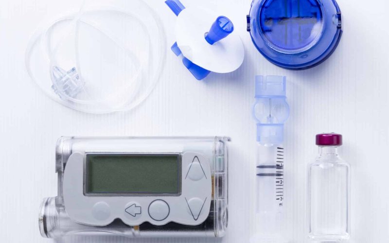 top view of an insulin pump set background consisting of: an insulin pump, insertion system of the infusion set, a reservoir of an insulin pump, insulin vial and a infusion set on a white background