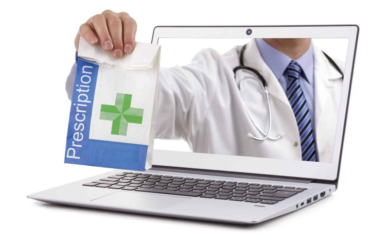 Internet drug store concept doctor holding prescription medicine through a laptop screen