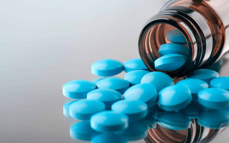 closeup of the desk of a doctors office with a bottle with pills in the foreground and a stethoscope in the background