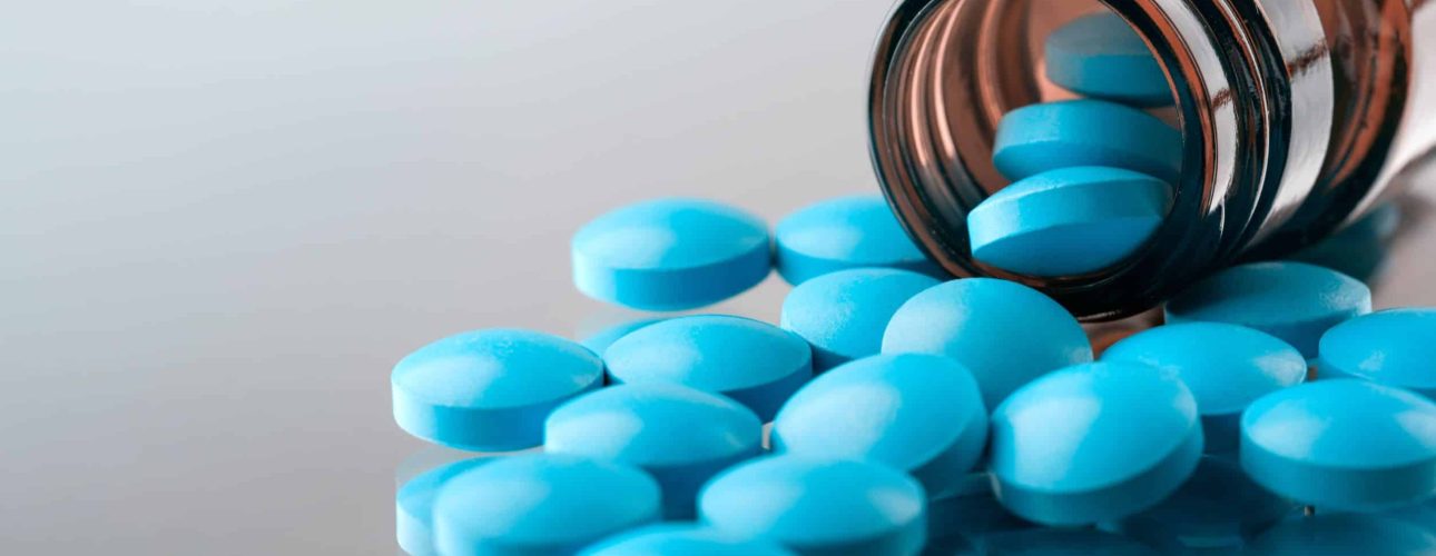 closeup of the desk of a doctors office with a bottle with pills in the foreground and a stethoscope in the background