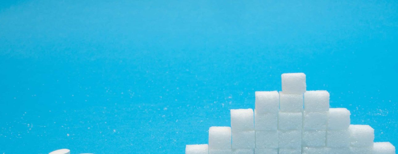 small pills of sugar replacement vs neat pile of refined sugar. natural vs chemical concept on blue background