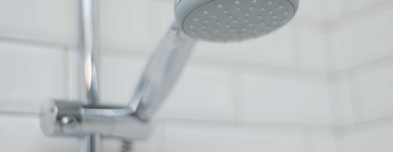 Close-up of chrome shower in the bathroom covered decorative ceramic tiles with white glossy bricks