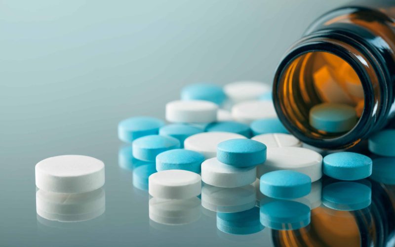 closeup of the desk of a doctors office with a bottle with pills in the foreground and a stethoscope in the background