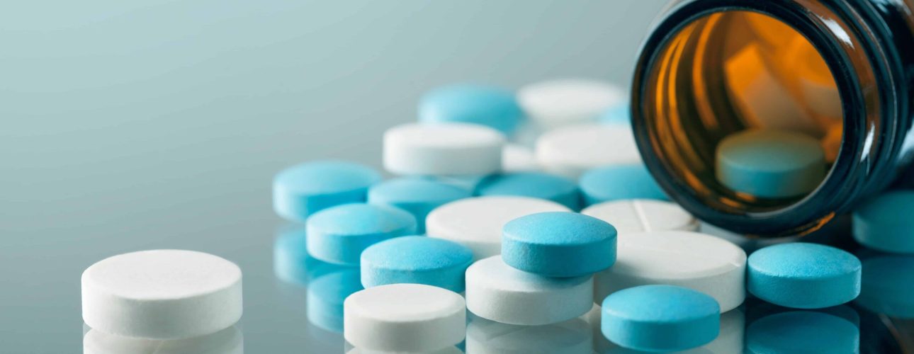 closeup of the desk of a doctors office with a bottle with pills in the foreground and a stethoscope in the background