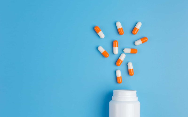 White and orange pills, tablets and white bottle on blue background.  Copy space for text