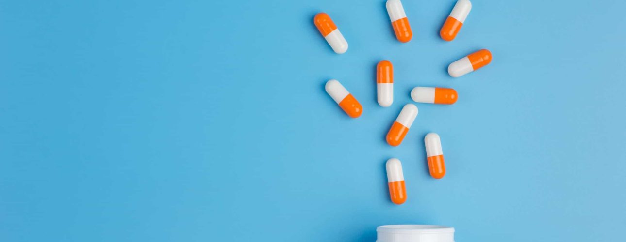 White and orange pills, tablets and white bottle on blue background.  Copy space for text