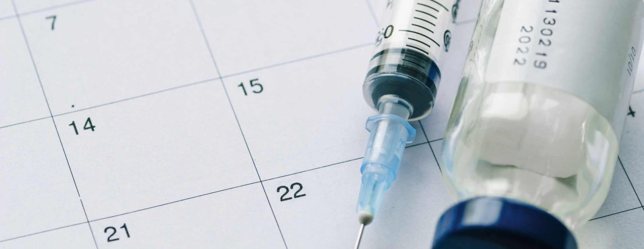 The vial with vaccine and syringe on calendar background, as a concept of vaccination season and date.