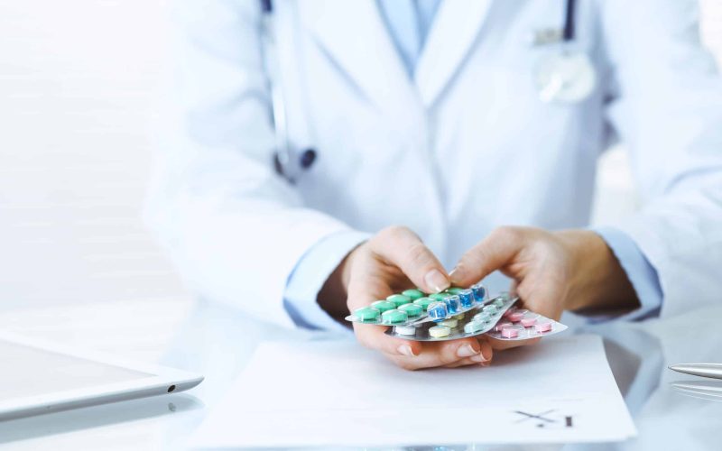 Unknown woman doctor at work at hospital. Pills at medical clipboard. Young female physician write prescription or filling up medical form while sitting in hospital office, close-up.