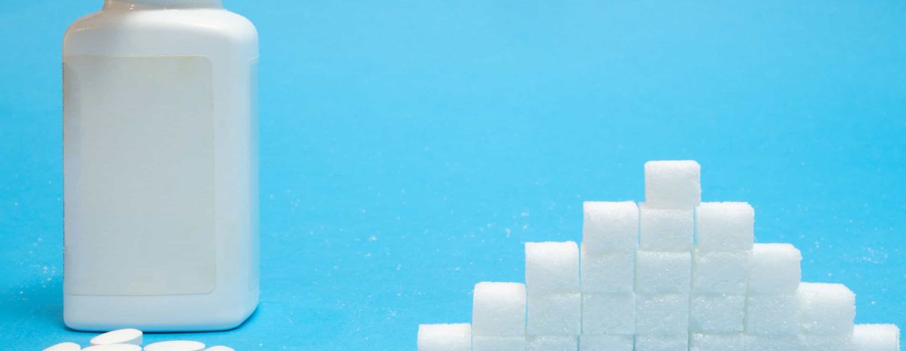 white tablets pills of sugar substitute sweetener with big bottle blank label vs pile of refined normal sugar concept on blue background