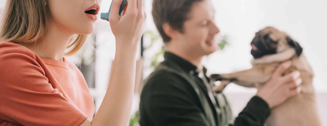 selective focus of attractive blonde woman allergic to dog using inhaler near man with pug