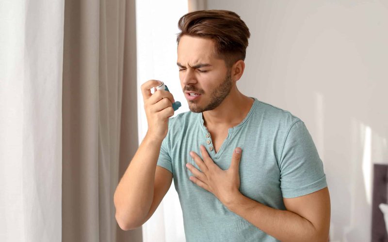 Young man using asthma inhaler at home