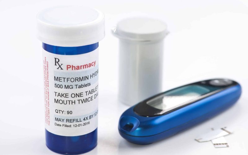 Metformin prescription bottle, glucometer and test stips.  Metformin is a generic medication name and label was created by photographer.