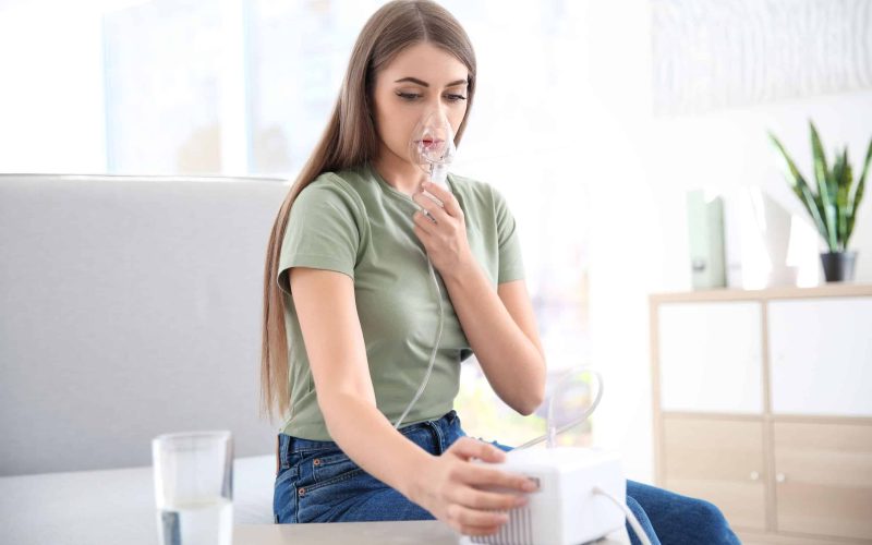 Young woman with asthma machine in light room