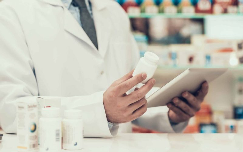 Closeup of a Pharmacist Holding Pills Bottle and Tablet.