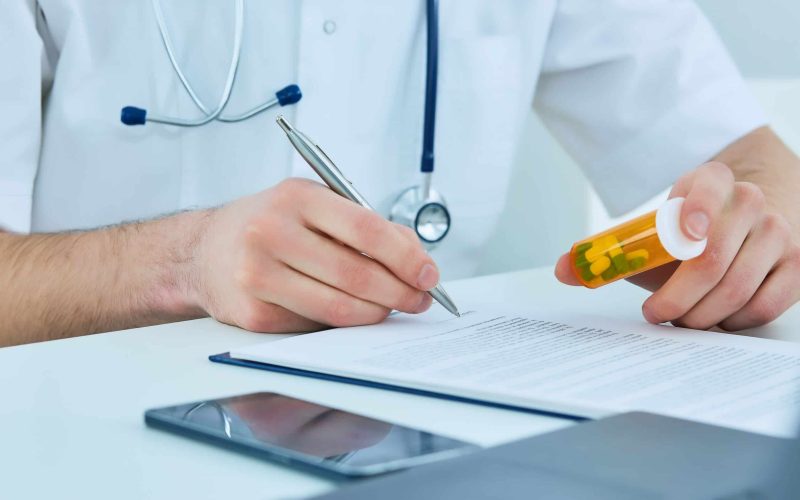 Close up of male doctor writing prescription paper and capsules