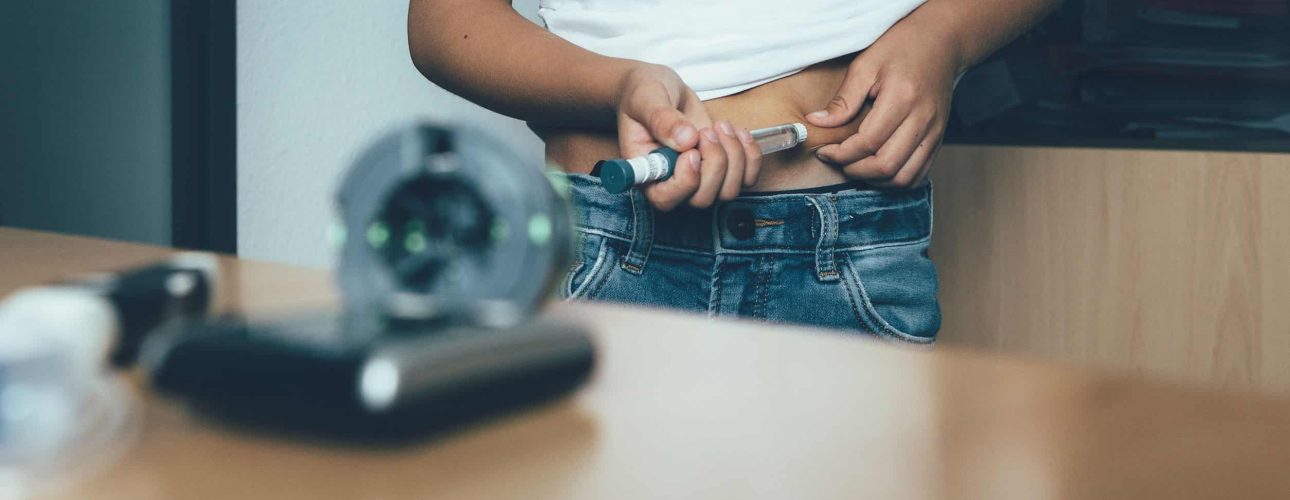 Cropped view of the abdomen of a diabetic child is injecting insulin with an insulin pen in the doctor office. Child diabetes concept