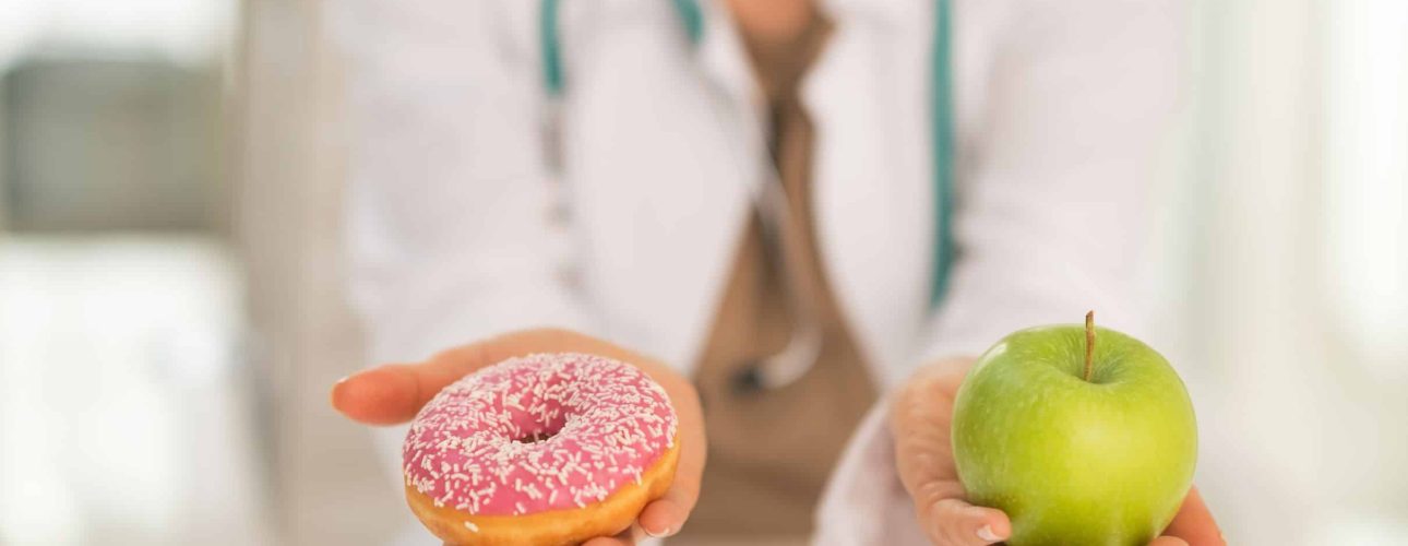 Closeup on medical doctor woman giving a choice between apple and donut