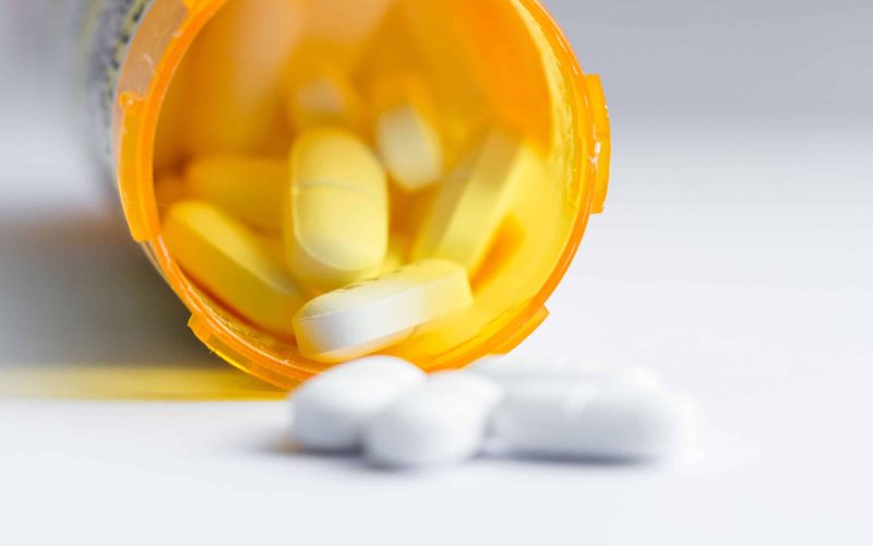 close up of a group of white tablets with an out of focus prescription bottle in the background