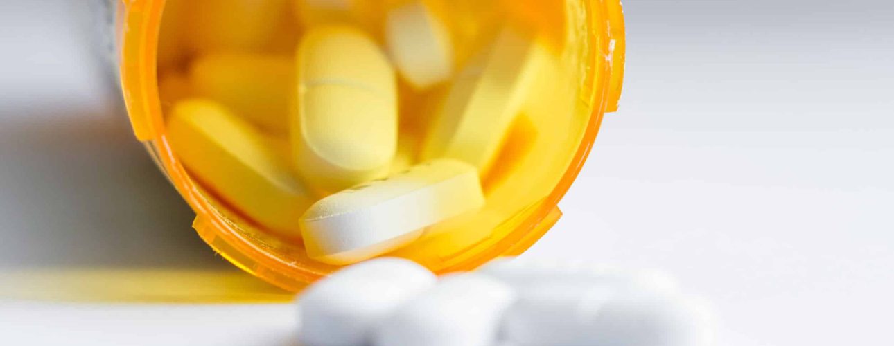 close up of a group of white tablets with an out of focus prescription bottle in the background