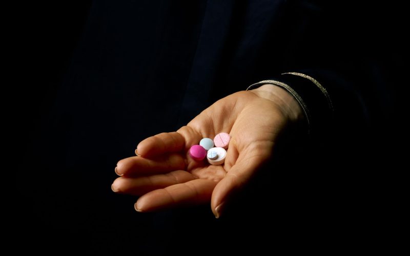 Black Mania. woman hand isolated on black showing pills