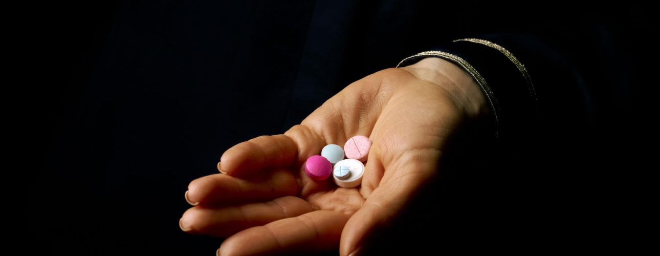 Black Mania. woman hand isolated on black showing pills