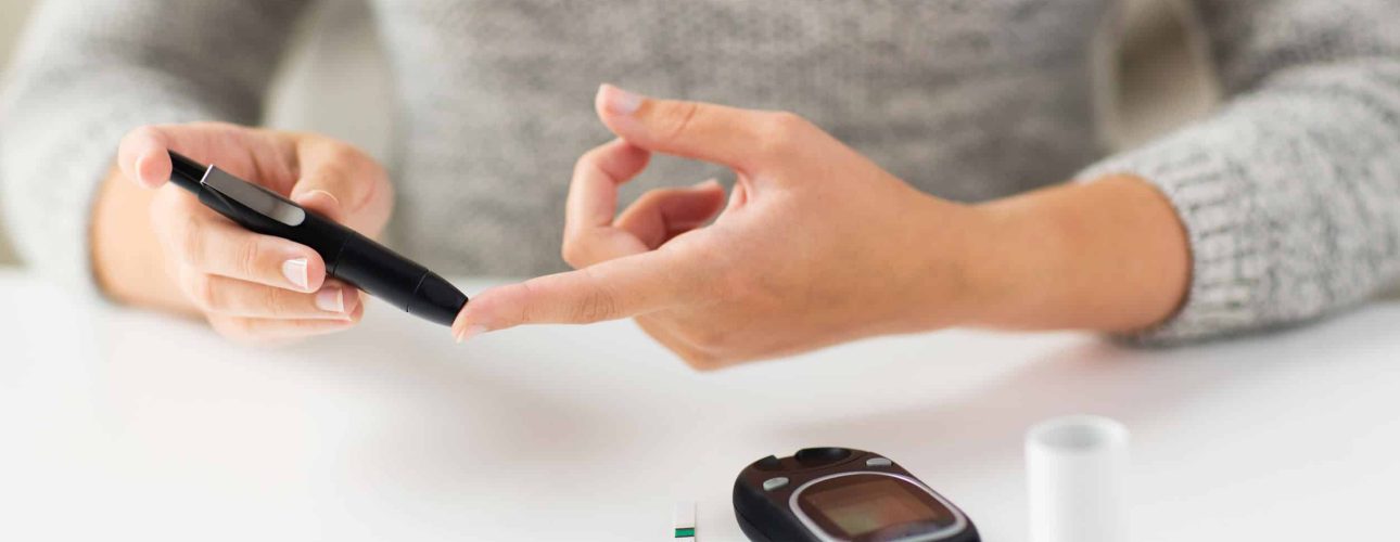 medicine, diabetes, glycemia, health care and people concept - close up of woman checking blood sugar level by glucometer at home