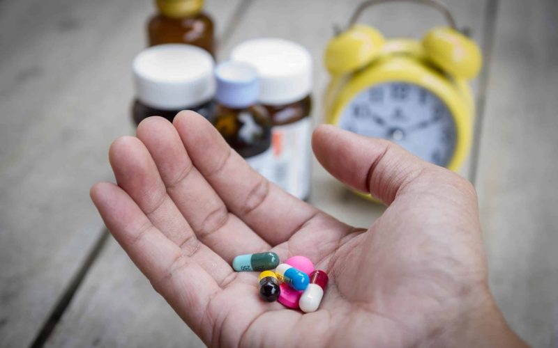 48070849 - man's hand hold many medicine, boxes of medicines and clock in the background