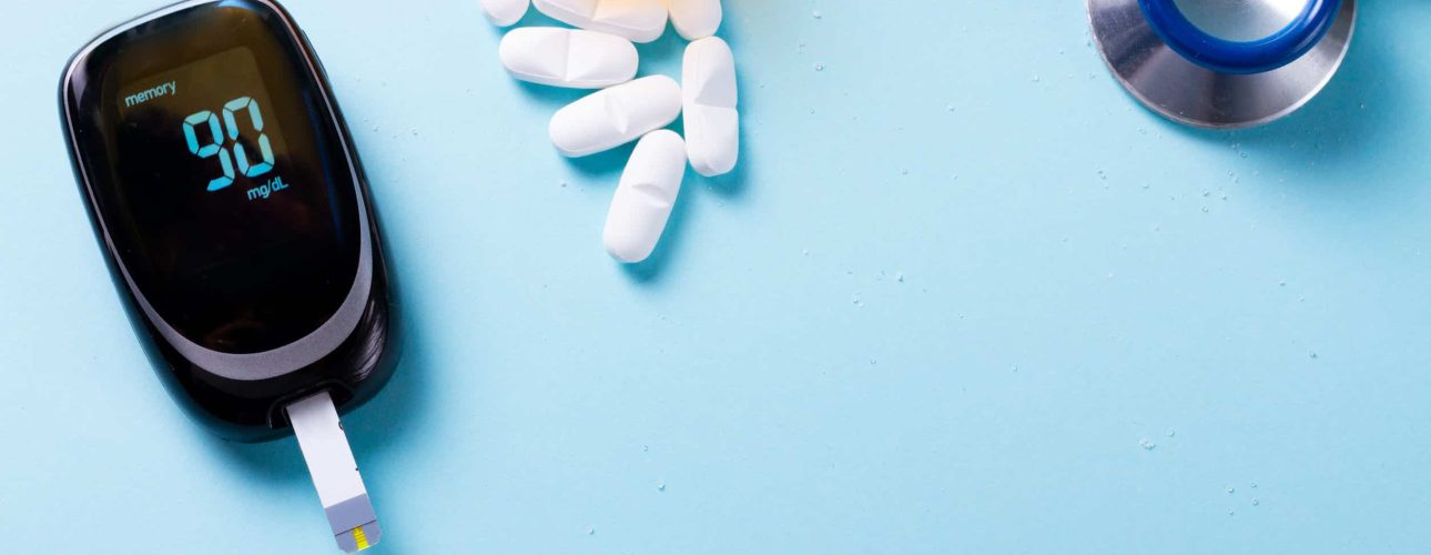 White pills in orange bottle with blood glucose meter on blue background with copy space