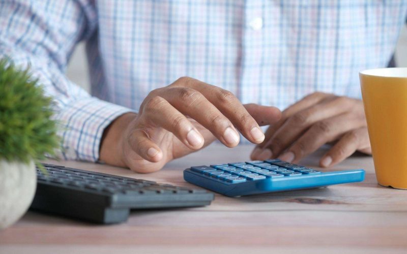 Person using a blue calculator at a desk to work out how to get Eliquis cheaper