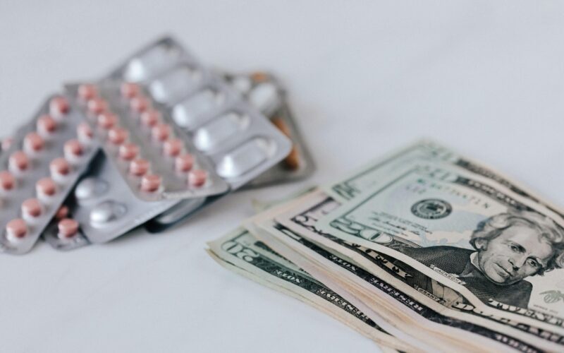 a pack of pills and money representing prescription drug prices increase many Americans face.