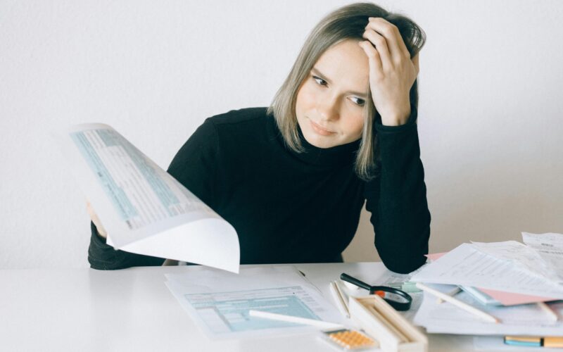 A woman looks stressed over a mess of paperwork because her medication isn't covered by insurance