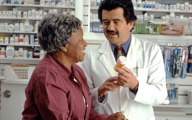 Pharmacist showing a patient a bottle of prescriptions and explaining how to save on prescriptions